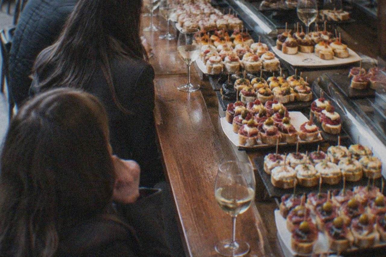 A busy pintxos bar counter in Bilbao loaded with small skewered bites and glasses of txakoli wine