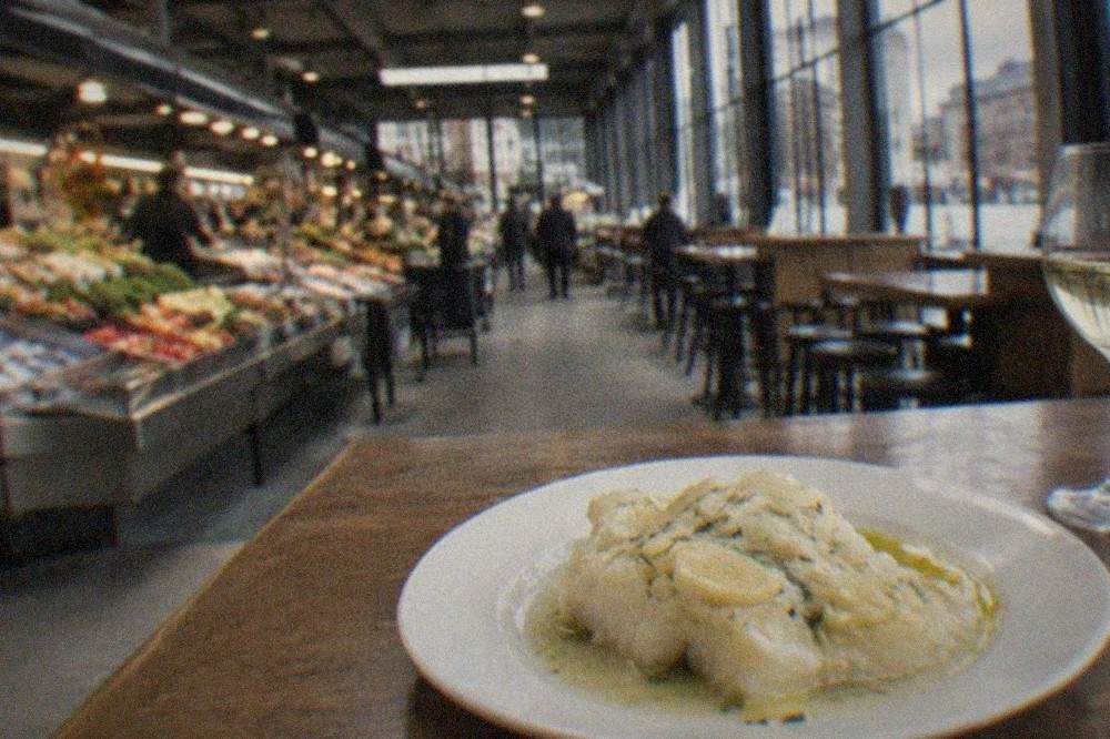 A close view of a plate of bacalao al pil pil, salt cod in a pale garlic emulsion, on a bar table
