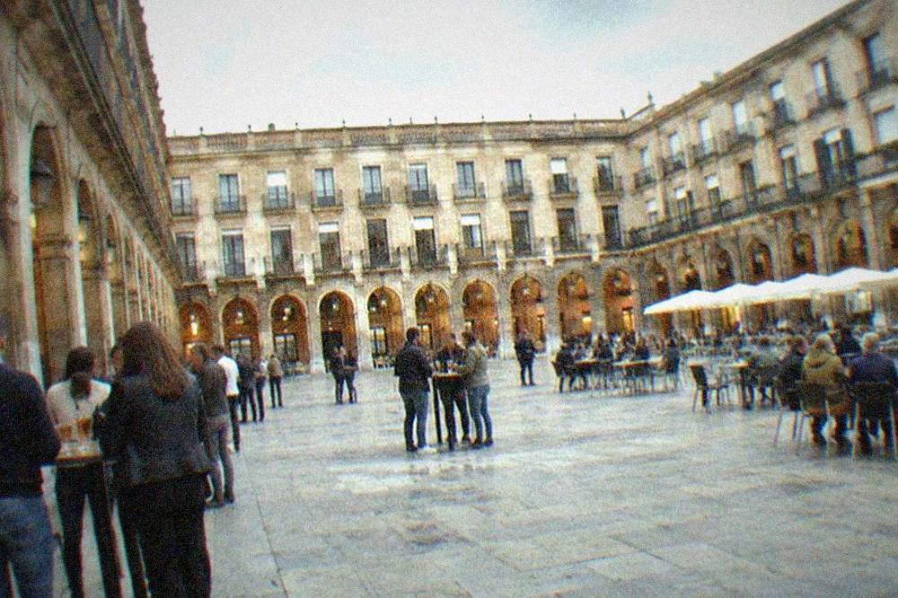 The arcaded Plaza Nueva in Bilbao with people standing at outdoor bar tables in the evening
