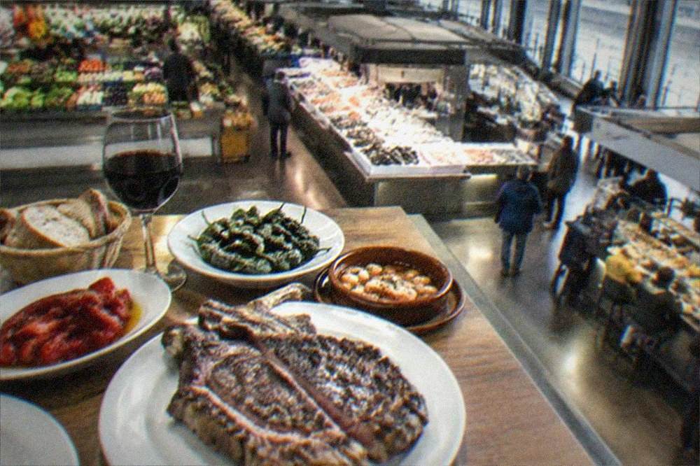 A table spread with Basque dishes including a large grilled txuleta steak and roasted peppers