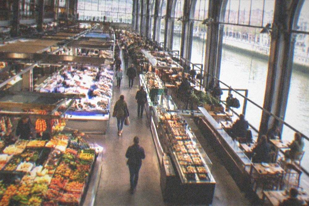 The interior of Mercado de la Ribera with market stalls and a food court beside the river