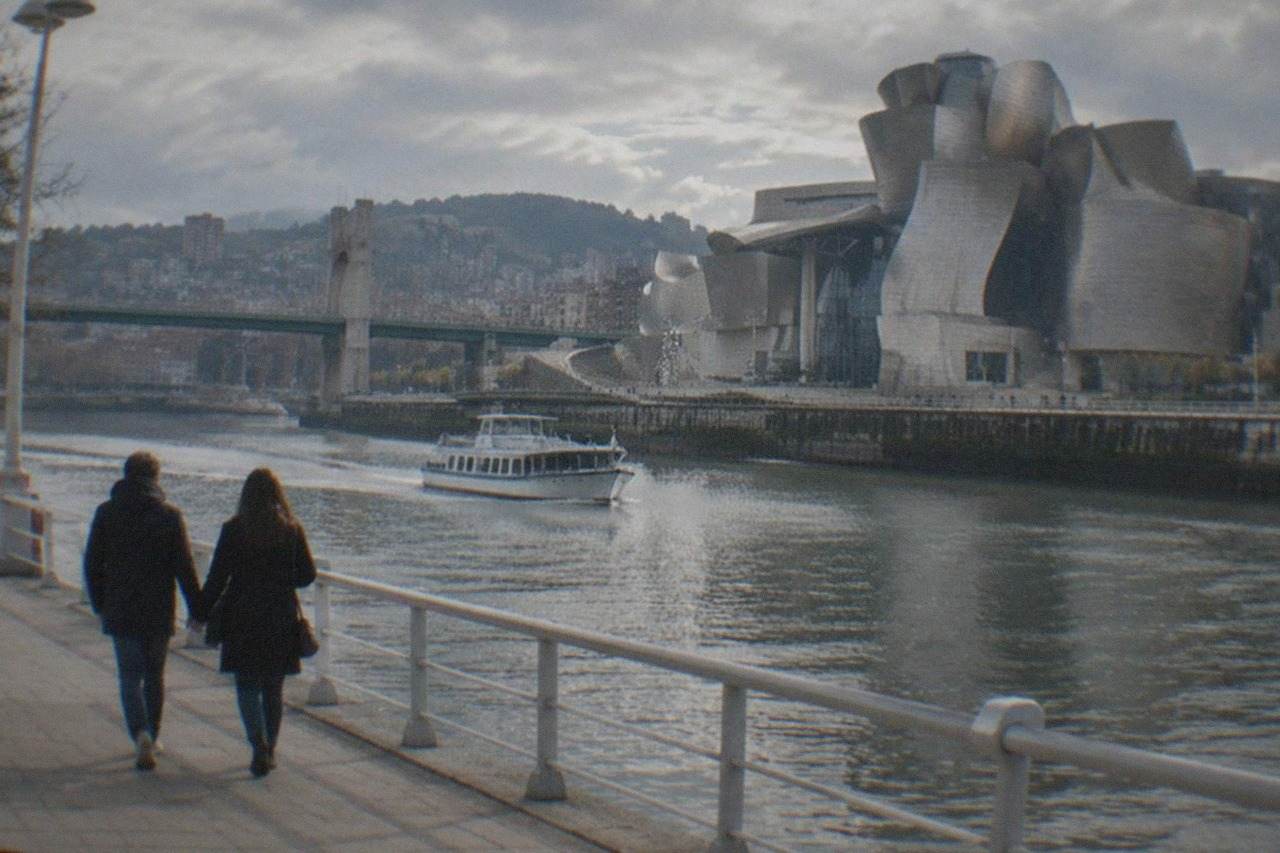 A couple walking hand in hand along the Nervion riverfront in Bilbao with the Guggenheim Museum in the background