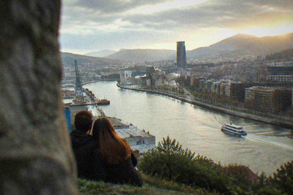 A couple on the Artxanda hillside viewpoint looking out over the Bilbao skyline and the Nervion river at sunset