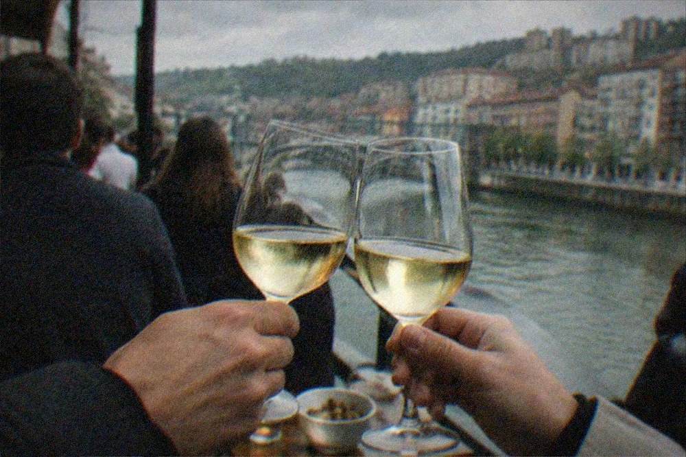 Two people toasting with glasses of txakoli wine at a crowded evening bar in central Bilbao