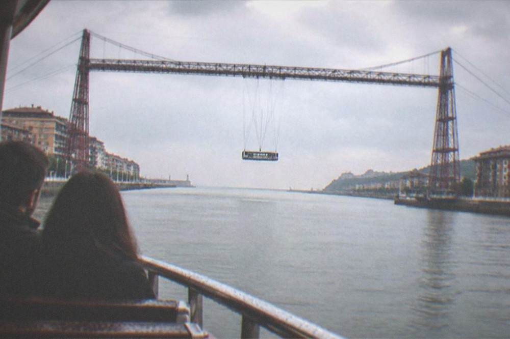 A couple sitting on a river boat looking up at the Vizcaya transporter bridge near Portugalete