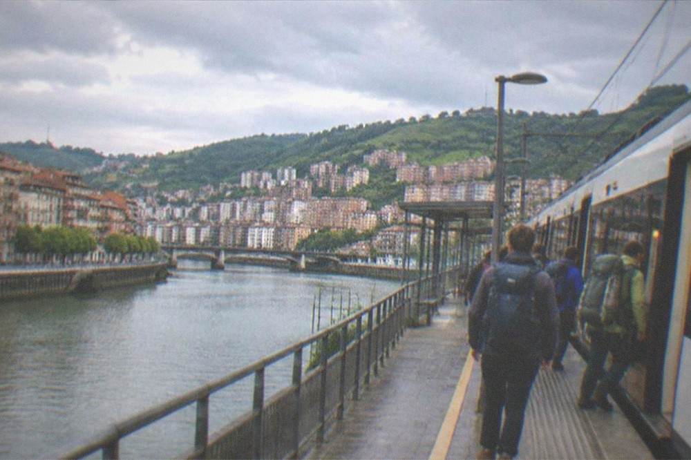 A train station platform beside a coastal Basque town with hikers boarding a commuter train
