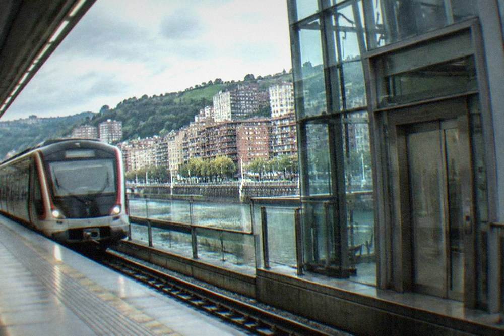 A Bilbao metro station platform with a train arriving beside elevator access doors