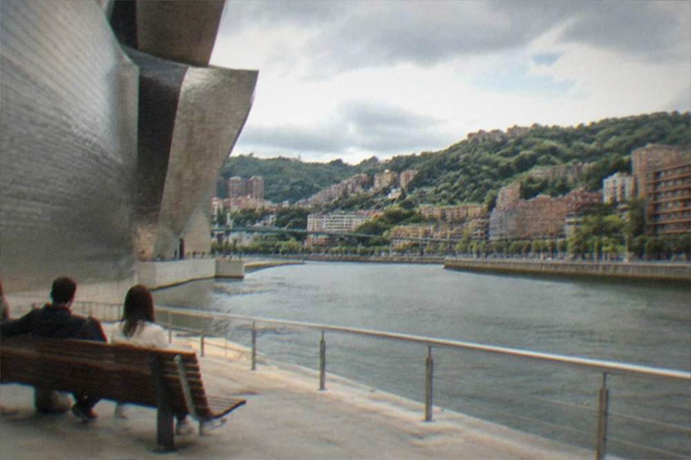 Visitors resting on a bench beside the Guggenheim Museum's curved titanium facade in Bilbao