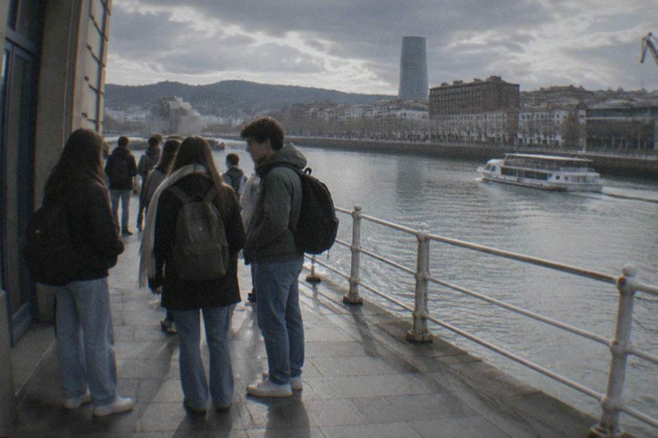 Students chatting outside a language school building on a Bilbao street with the Nervion river behind them