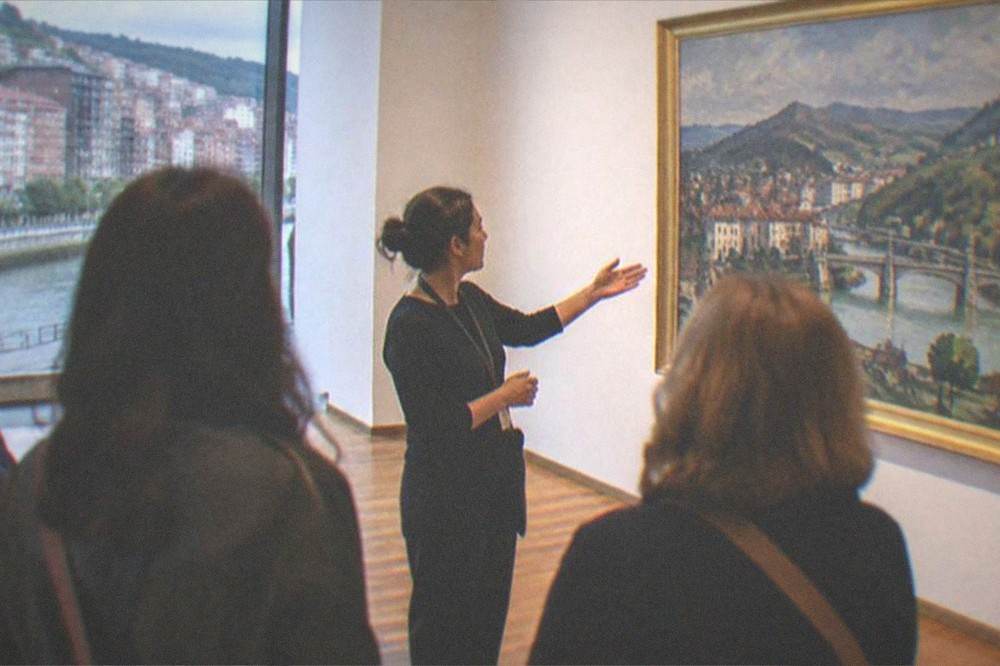 A guide explaining a painting to a small group inside a brightly lit museum gallery