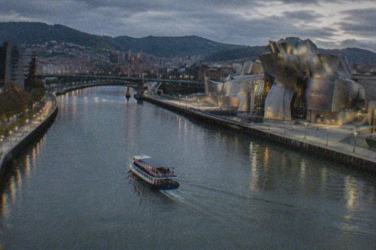 Evening view over Bilbao's Nervion river with the Guggenheim Museum titanium curves glowing under street lights