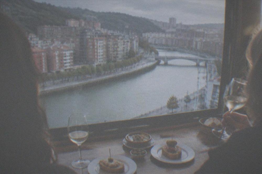 Two friends sharing pintxos and wine at a wooden bar counter in a traditional Bilbao tavern