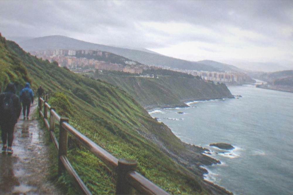 Travelers on a coastal path above the sea near Bilbao with green cliffs and blue water below