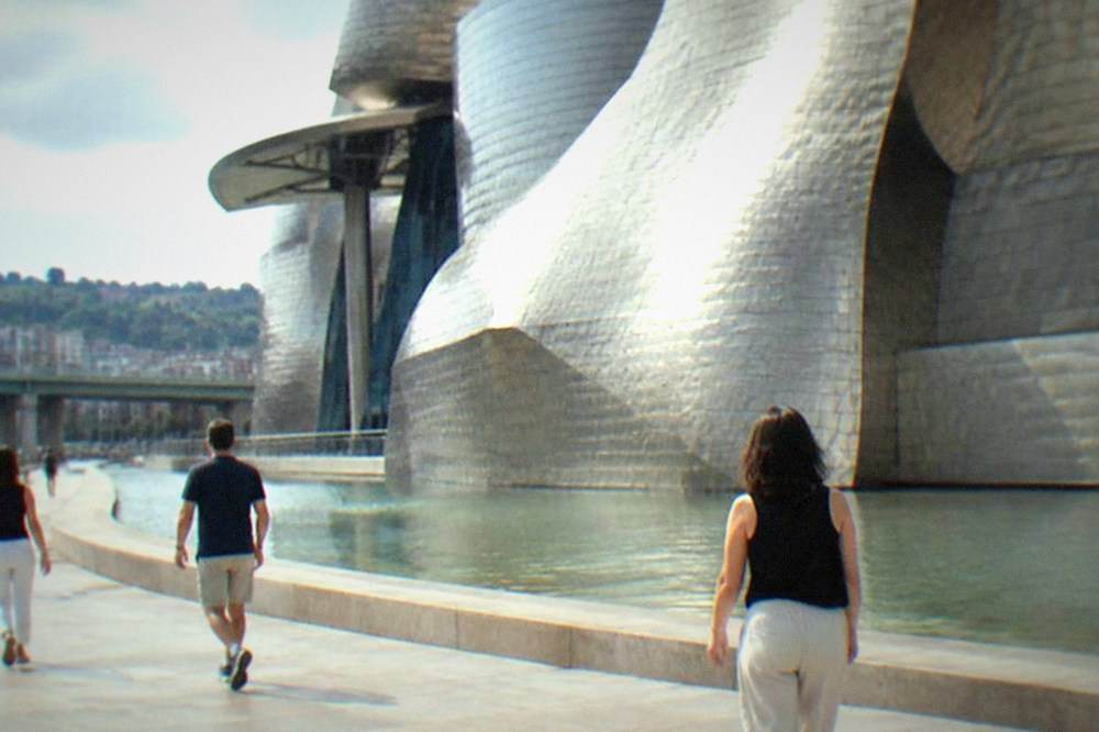 Visitors without bags walking past the titanium curves of the Guggenheim Museum on a sunny afternoon