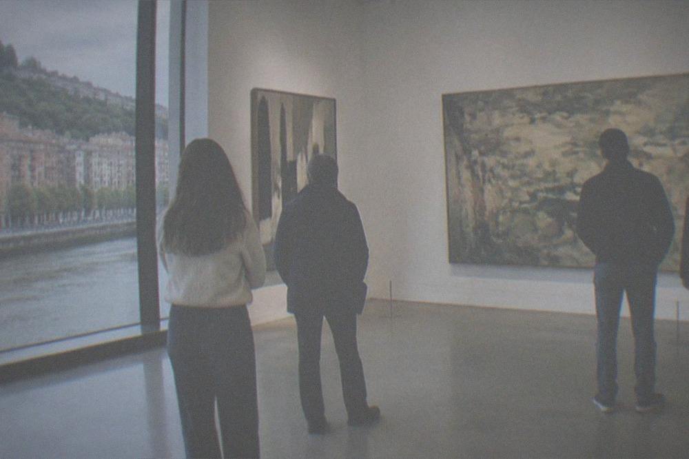 Museum visitors with no bags standing in front of large art displays inside a bright gallery