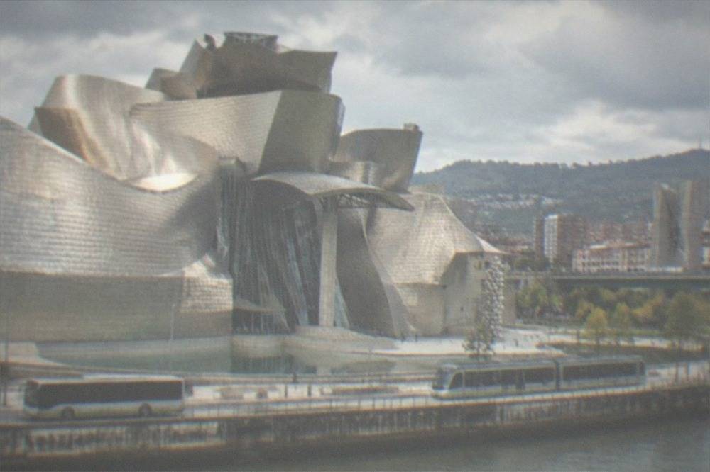 A low-floor Bilbao bus and a tram passing on a street near the Guggenheim Museum