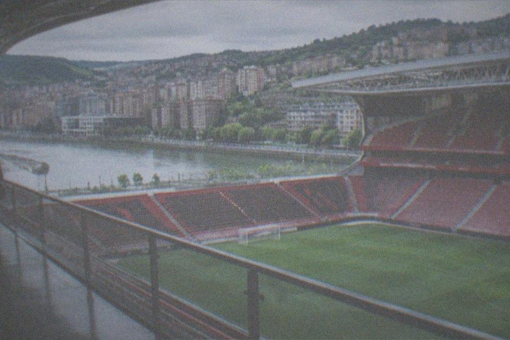 A football stadium interior with rows of seats and green pitch seen from a museum walkway