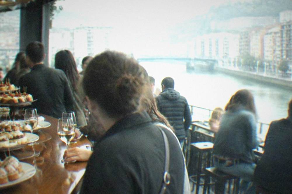 A crowded pintxos bar counter in Bilbao with plates of small bites and glasses of txakoli wine