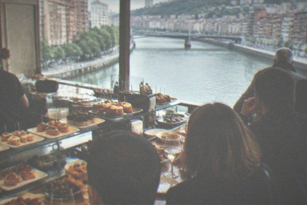A crowded pintxos bar counter with small plates and glasses of txakoli