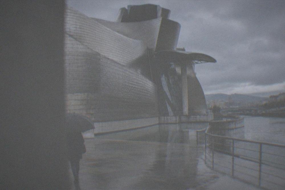 A visitor holding an umbrella while walking past the Guggenheim Museum on a drizzly day