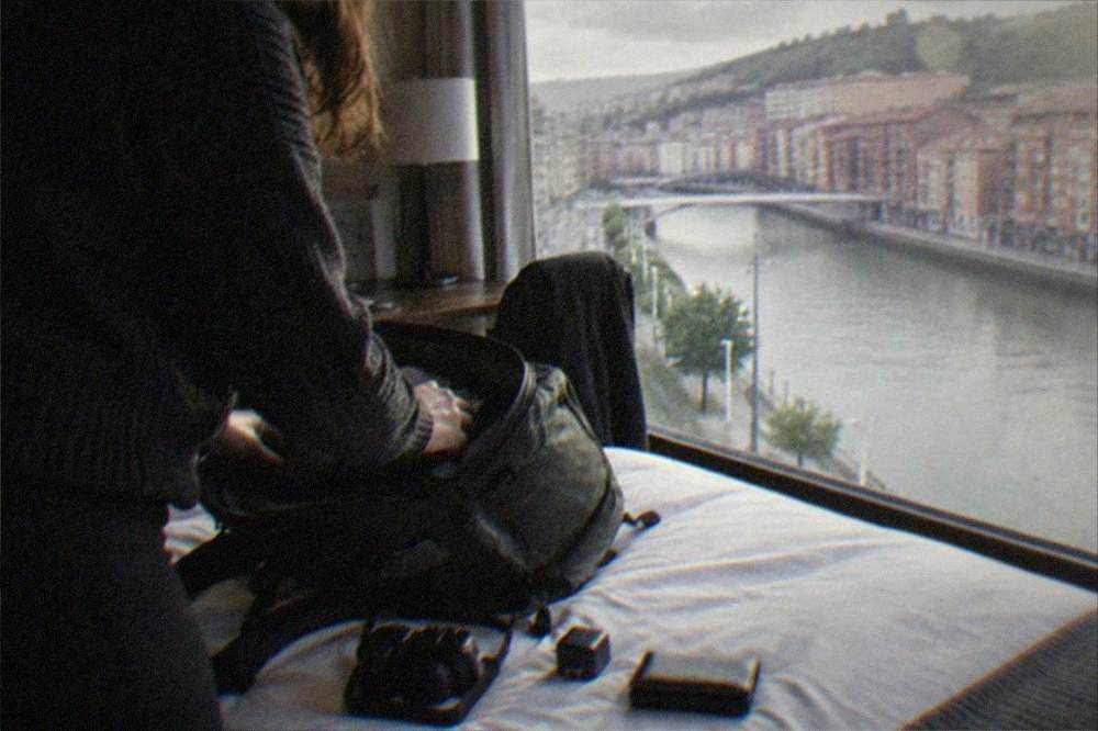 Traveler packing a small daypack with a camera, adapter and wallet on a hotel bed