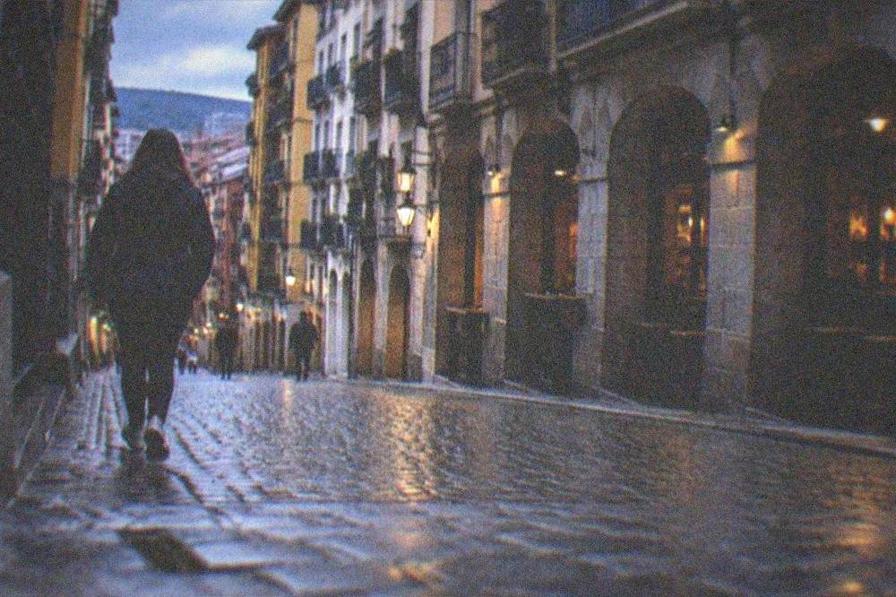 A traveler walking a steep cobblestone lane in Bilbao's Casco Viejo wearing sneakers and a rain jacket