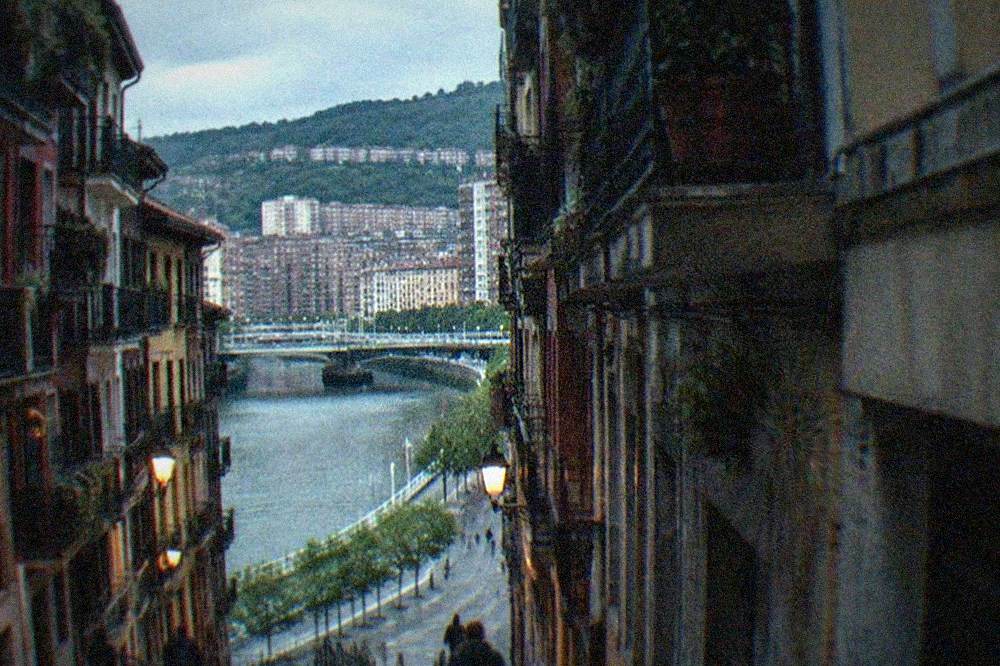 A narrow Old Town street in Bilbao with balconies, bar signs and a few pedestrians