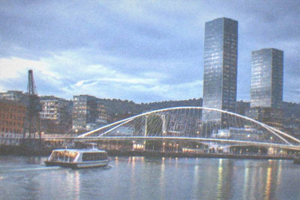 A white footbridge over the Nervion river with glass towers behind at blue hour