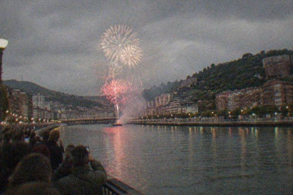 Night crowd gathered along the Bilbao riverside watching fireworks over the estuary