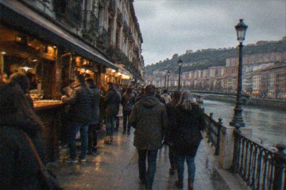 People strolling past pintxos bars with crowded counters in Bilbao's old town in the evening