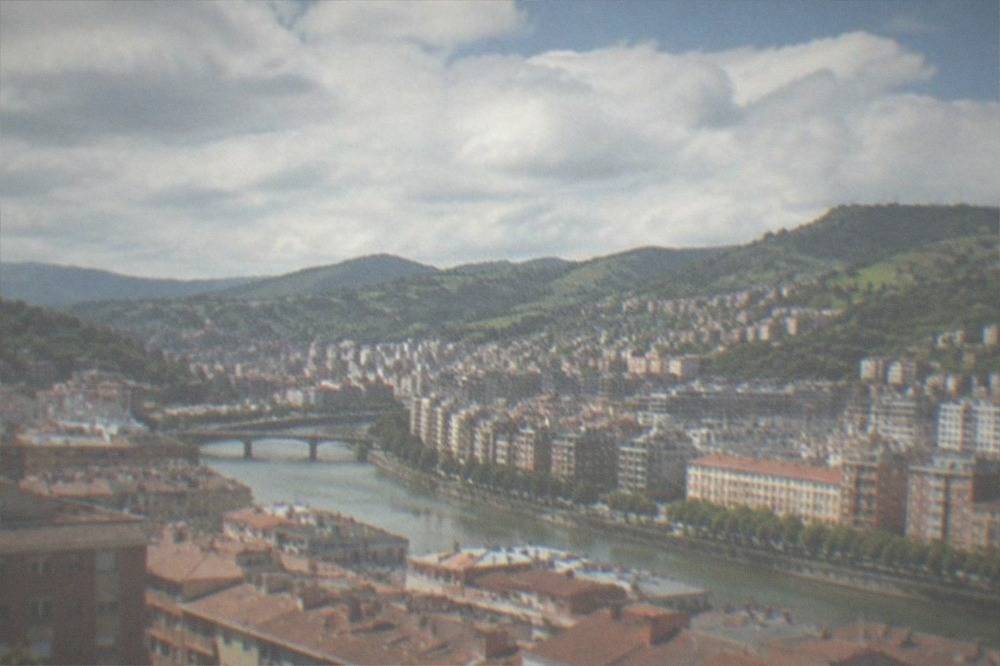 View over Bilbao rooftops toward the green hills surrounding the city on a clear day