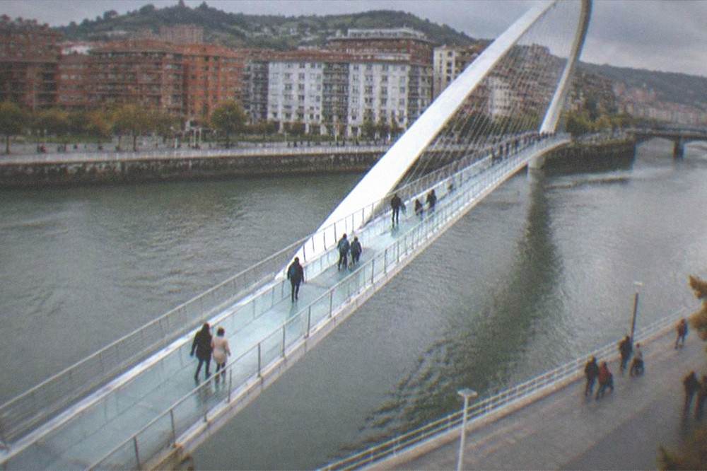 Families and locals walking along the Bilbao riverside promenade near the Zubizuri bridge