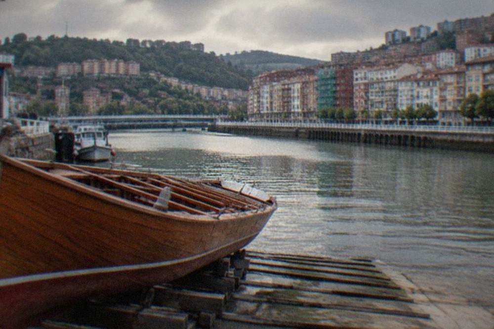 A wooden trainera racing boat resting on a slipway beside a Basque fishing harbour