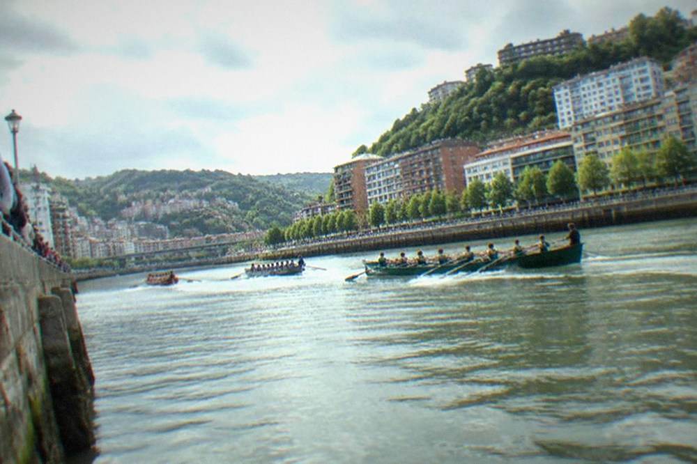 Spectators lining a harbour wall watching racing boats pass in a Basque coastal town