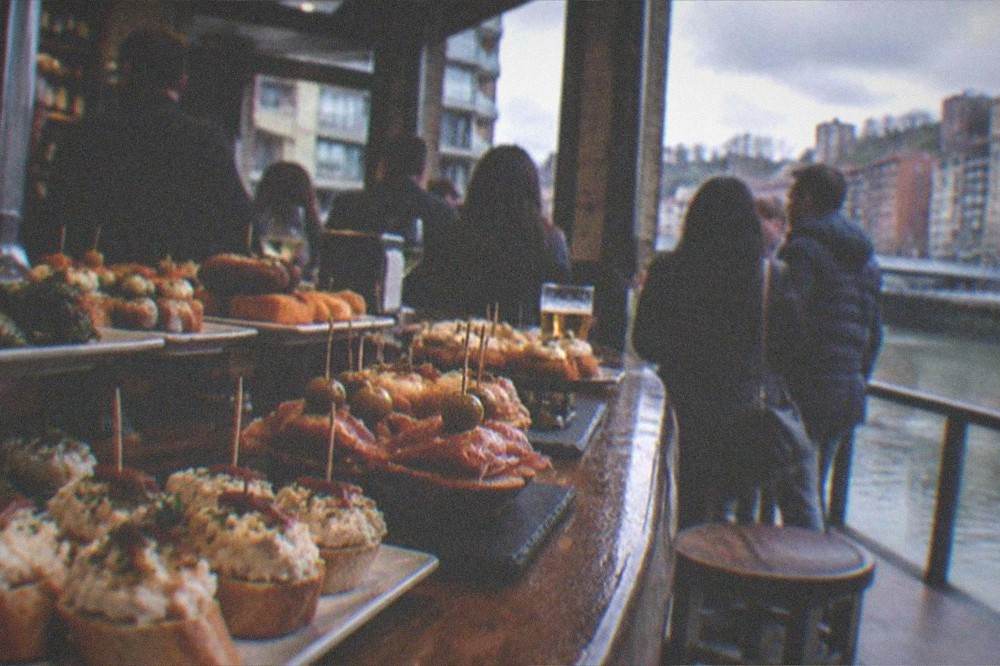 Pintxos arranged on a bar counter in a crowded Bilbao tavern