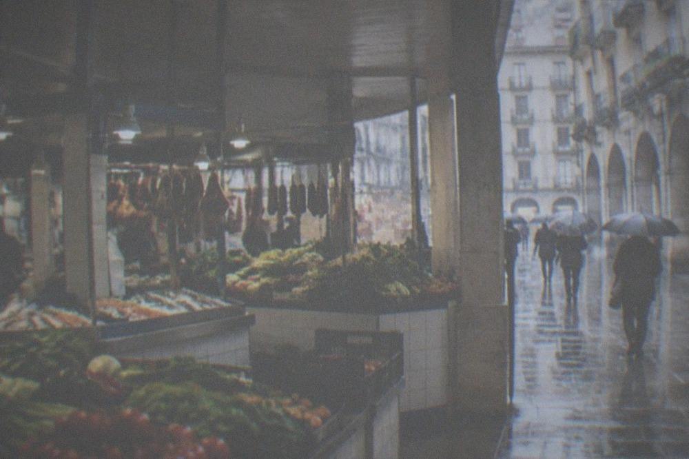 People with umbrellas walking along an arcaded old town street in light rain