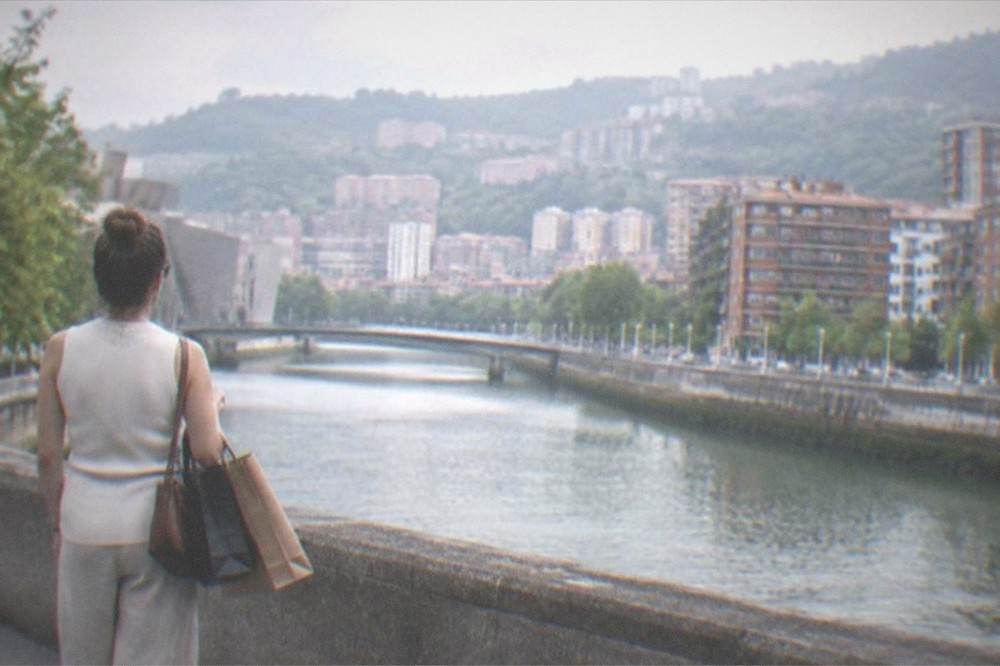 A shopper carrying paper bags from boutiques pausing at a plaza edge in Bilbao