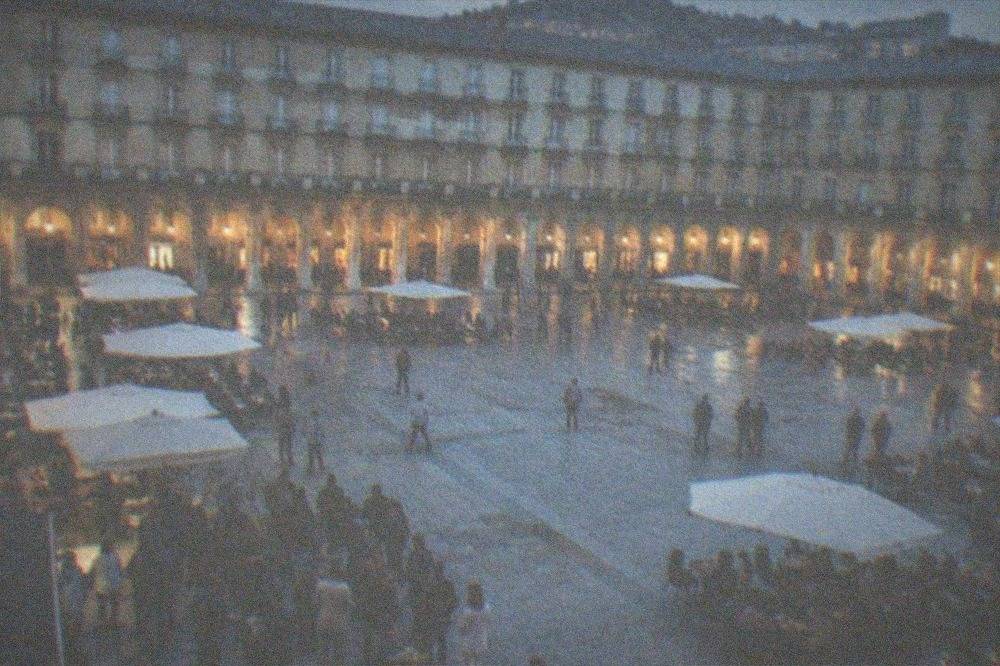 Crowd standing with small plates and drinks at a Plaza Nueva bar in the evening