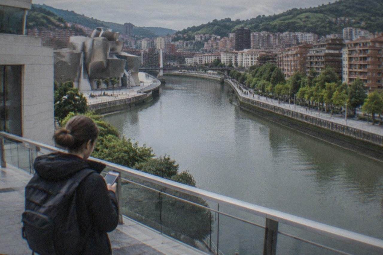 A traveler checking a smartphone outside a modern building in Bilbao