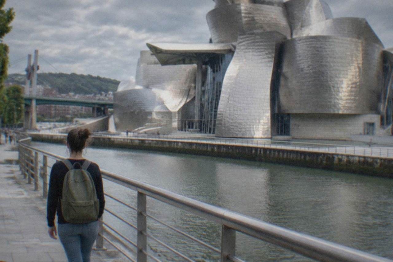 A woman with a backpack walking along the riverside promenade beside the Guggenheim Museum in Bilbao