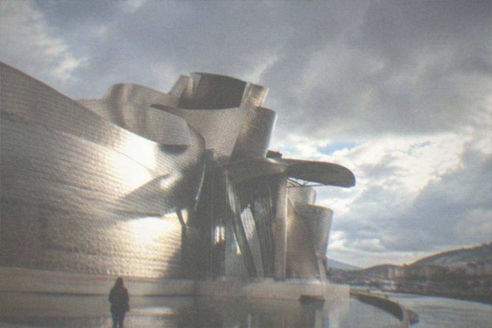 A visitor standing alone in front of the titanium curves of the Guggenheim Museum Bilbao