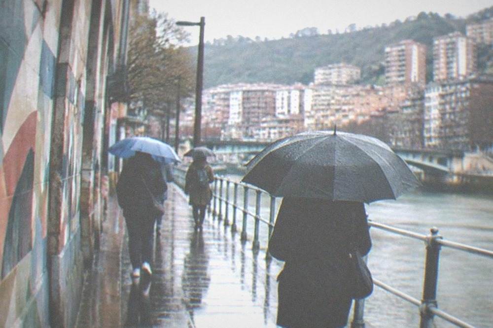 People walking with umbrellas past painted walls on a rainy afternoon in a Bilbao street