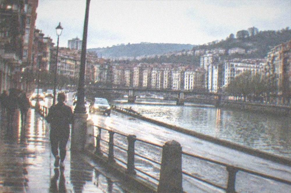 Rain-soaked Bilbao street at night with headlights reflecting on wet pavement