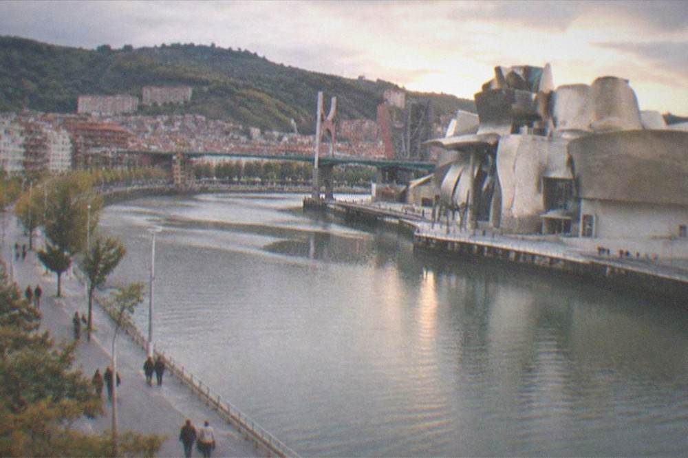 Pedestrians walking along the riverside promenade in Bilbao with the Guggenheim Museum in the distance