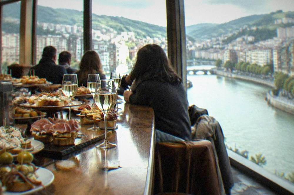 Pintxos and glasses of txakoli lined along the counter of a crowded Bilbao bar
