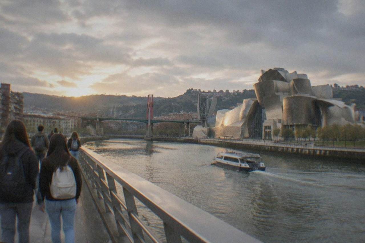 Students walking across a bridge over the Nervion river with the Guggenheim Museum in the background