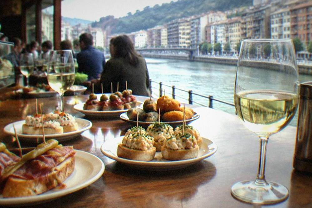 Crowded pintxos bar counter in Bilbao with plates of small snacks and glasses of txakoli wine