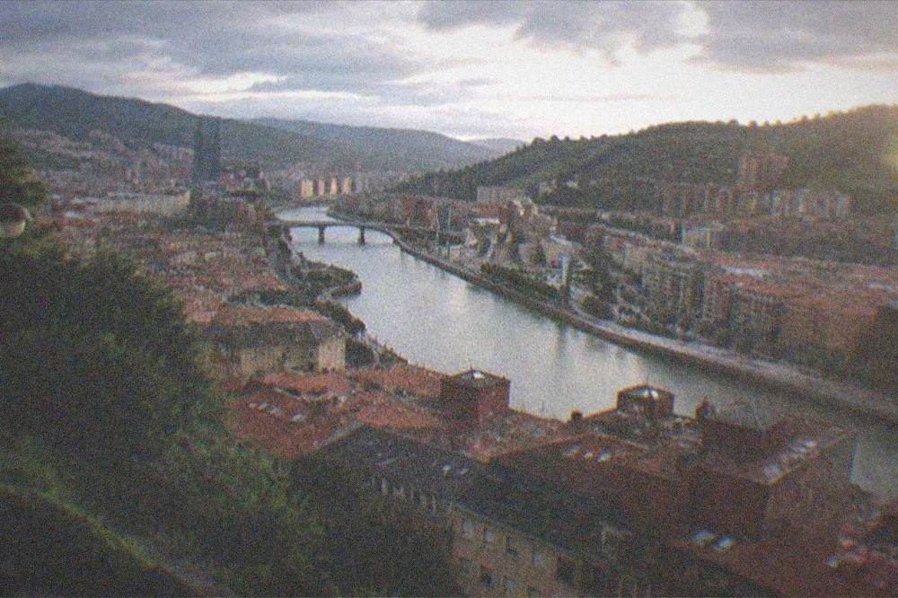 Evening view over Bilbao rooftops toward the river and distant green hills