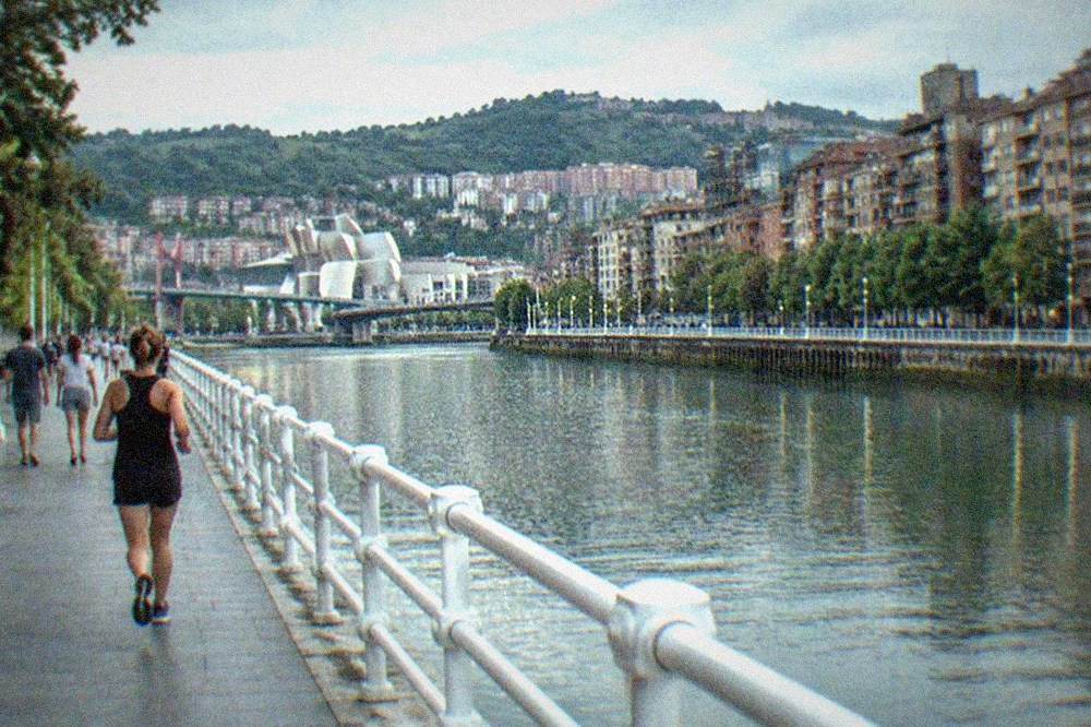 Visitors walking along the Bilbao riverside promenade in warm summer sunshine