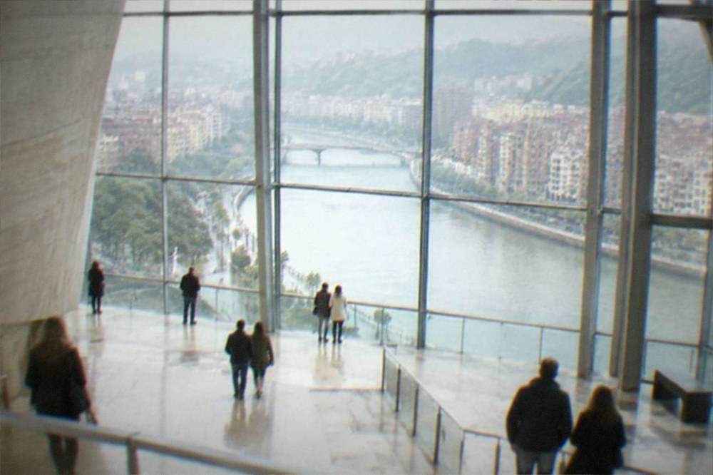 Visitors inside the bright atrium of a Bilbao museum on a rainy day